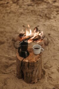 Un cadre serein autour d'un feu de camp avec café et cafetière moka sur une bûche de bois, parfait pour les amoureux du plein air.