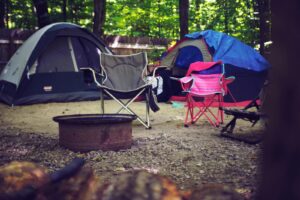 Un camping serein dans les bois avec des tentes colorées, des chaises de camping et un foyer, parfait pour une escapade de loisirs.
