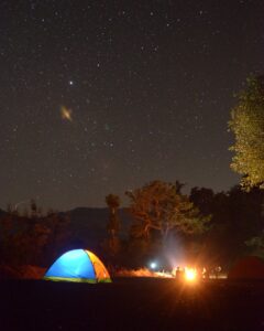 Camping en plein air sous un ciel étoilé avec une tente lumineuse et un feu de camp.