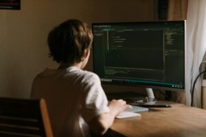 Un adolescent concentré sur le codage de logiciels sur un écran de bureau dans un environnement de bureau à domicile.