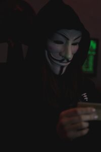 Individu anonyme portant un masque de Guy Fawkes utilisant un ordinateur portable, incarnant le secret et l'anonymat numérique.