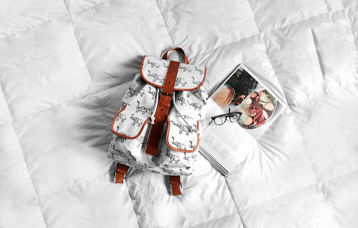 Sac à dos, livre et lunettes sur un lit