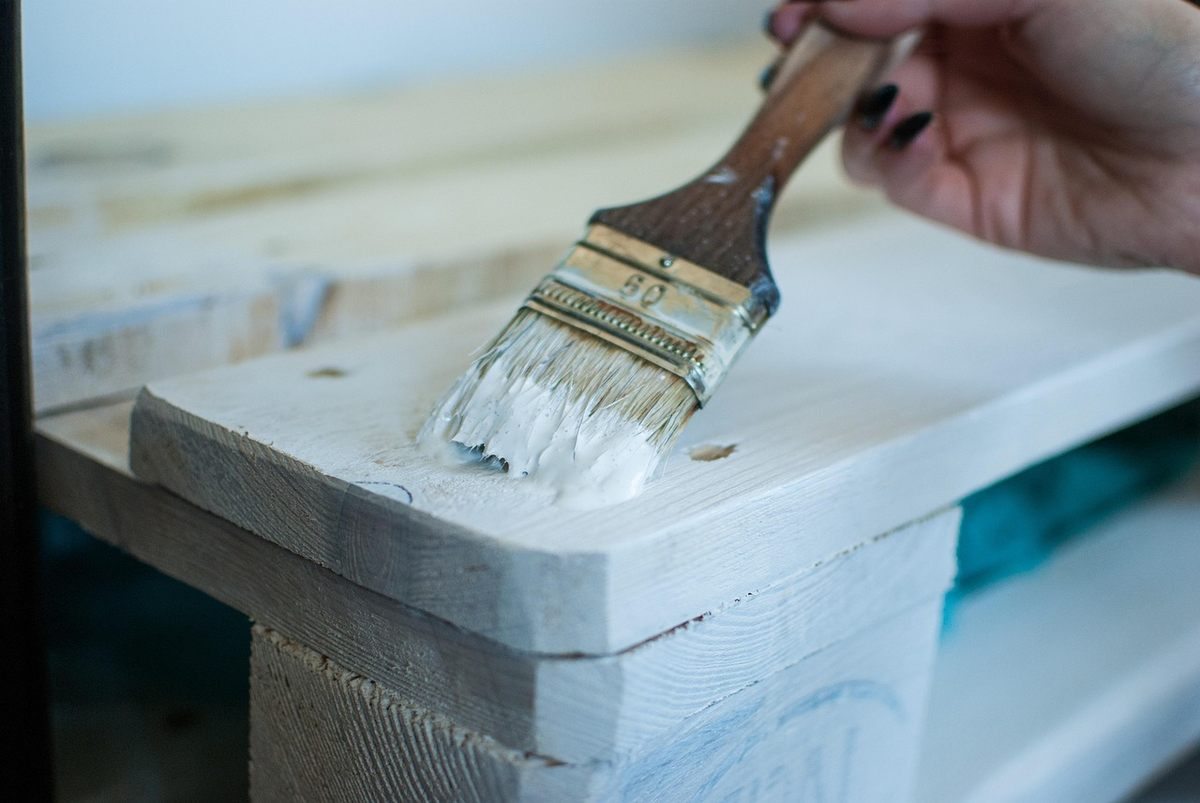 Main tenant un pinceau appliquant de la peinture blanche sur une surface en bois stratifiée