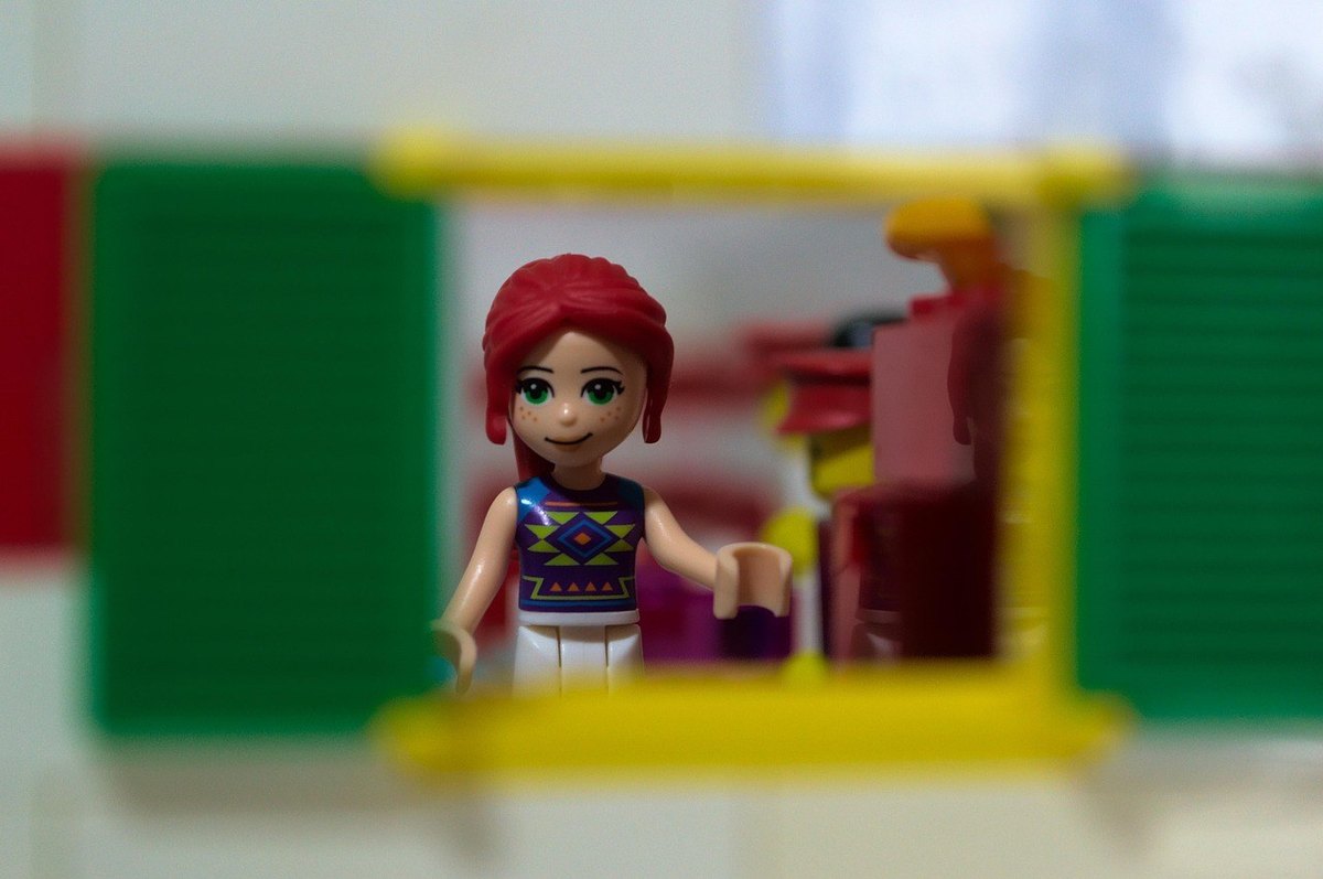 Figurine Lego d'une fille aux cheveux rouges dans une maison miniature devant une fenêtre